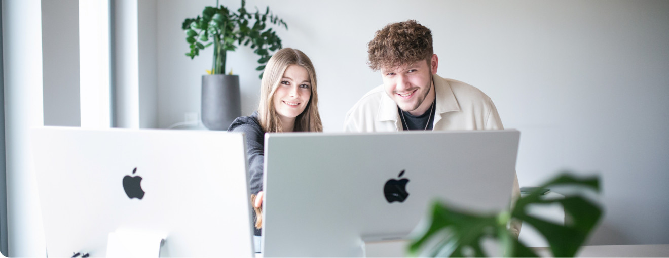 Junge Frau und junger Mann hinter Laptops lächelnd