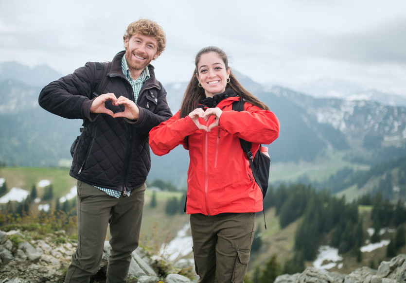 Mann und Frau auf Berggipfel zeigen mit den Händen Herzen